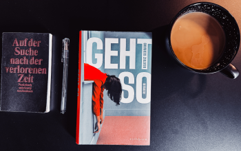 Links ein schwarzes Notizbuch mit Stift, in der Mitte das Buch "Geht so" von Beatriz Serrano, rechts eine schwarze Tasse mit Milchkaffee